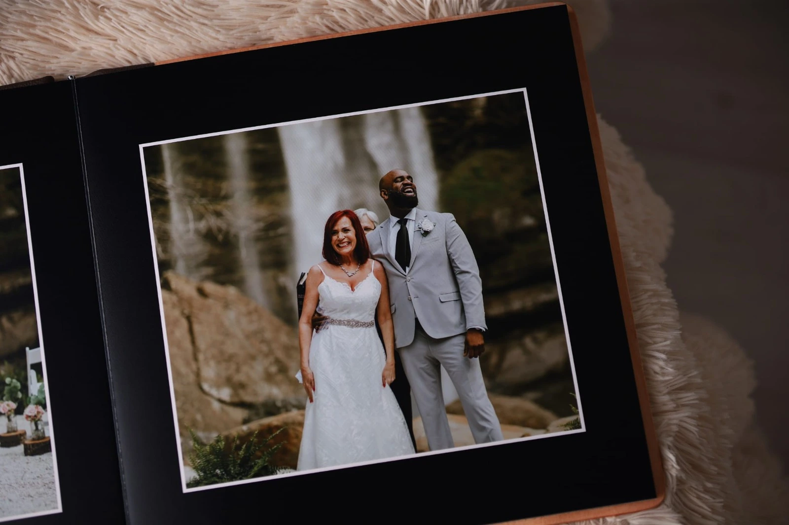 An anniversary photo album is open, showing a newlywed couple smiling in front of a waterfall. The bride wears a white gown, and the groom wears a light gray suit with a black tie.