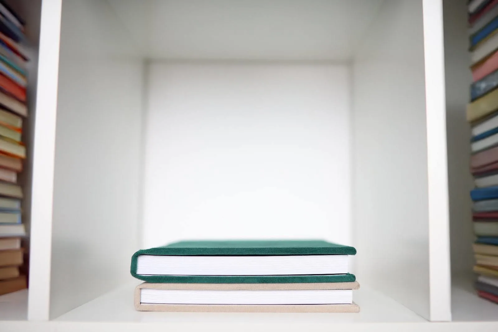Two photo albums stacked on a white bookshelf, surrounded by neatly organized books on either side.