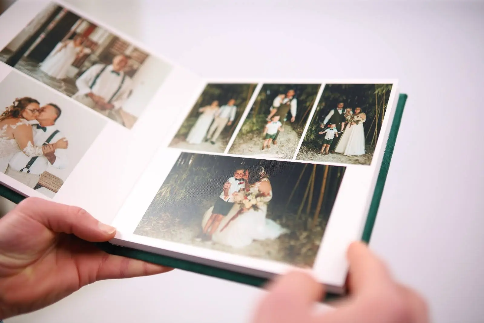 A person holding an open wedding photo album showing several pictures of a couple and family moments.