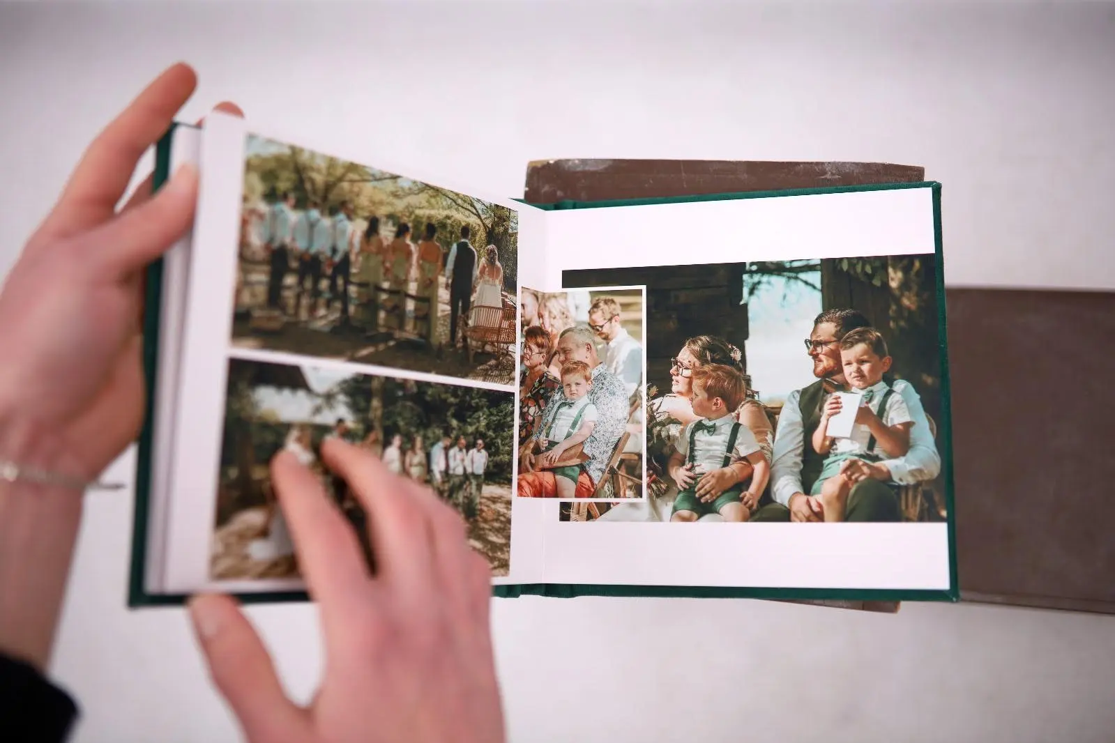 A person flipping through a wedding photo album showing group photos and family moments with children.
