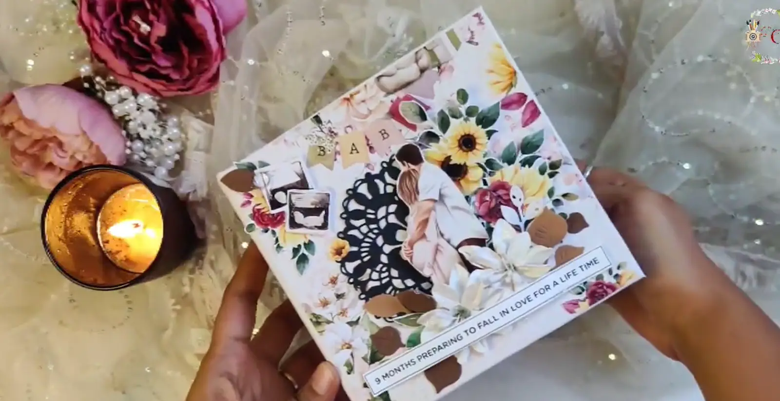 A decorated baby-themed photo album cover with flowers, parents hugging, and the text “9 months preparing to fall in love for a lifetime.”