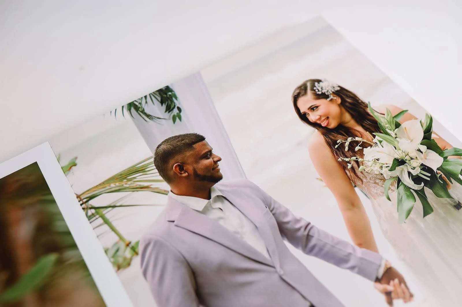 A bride and groom smiling at each other while holding hands during a beachside wedding ceremony.