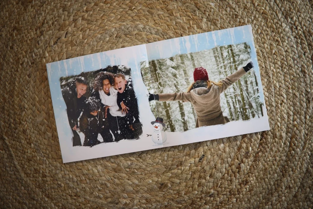 A photo book showing happy winter memories: friends playing in the snow and a woman in a red hat with arms wide open in a snowy forest.
