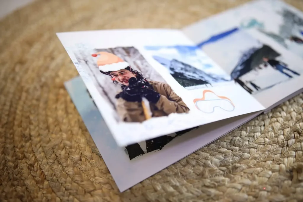 An open photo book with winter scenes, showing a smiling person in a Santa hat and snowy mountain pictures.