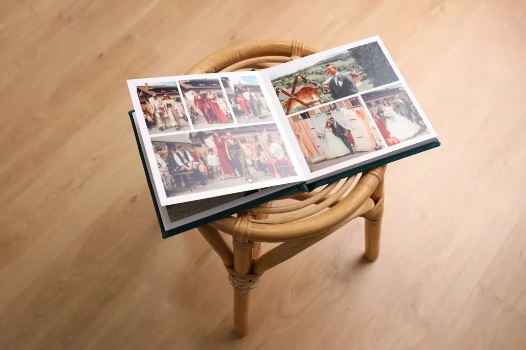 A photo album is placed open on a wooden chair, showing wedding photos. One side has group pictures of guests in formal attire, while the other features the groom and bride on their wedding day in scenic outdoor locations.